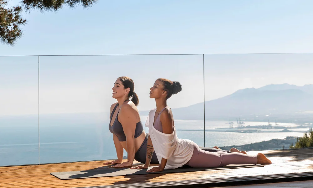 Two women practice yoga outdoors on a wooden deck