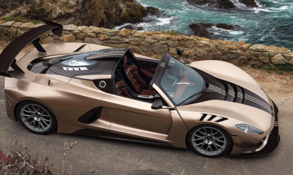 A sleek, metallic gold sports car with black accents is parked near a rocky coastline
