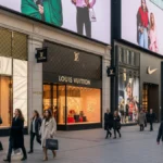 Shoppers walking past Gucci, Louis Vuitton, Nike, and Zara stores showcasing top fashion clothing brands