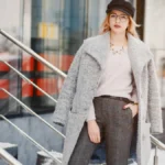Woman in fashionable winter attire stands confidently on snowy steps