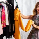 Smiling woman holding up a yellow dress from a clothing rack