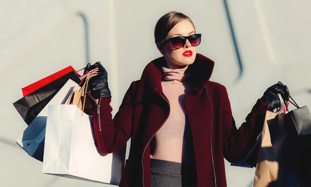 Woman in sunglasses and coat holding shopping bags