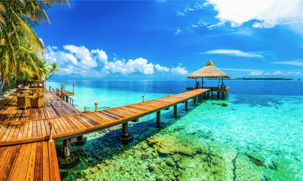 Wooden pier over clear turquoise water to a thatched hut