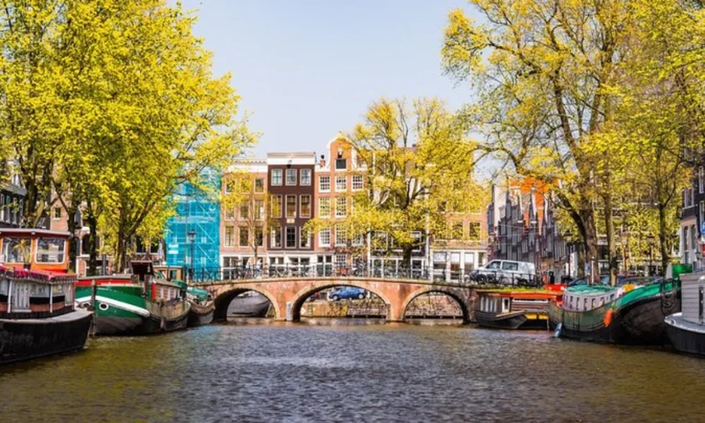 Amsterdam canal with boats, bridge, trees, and buildings