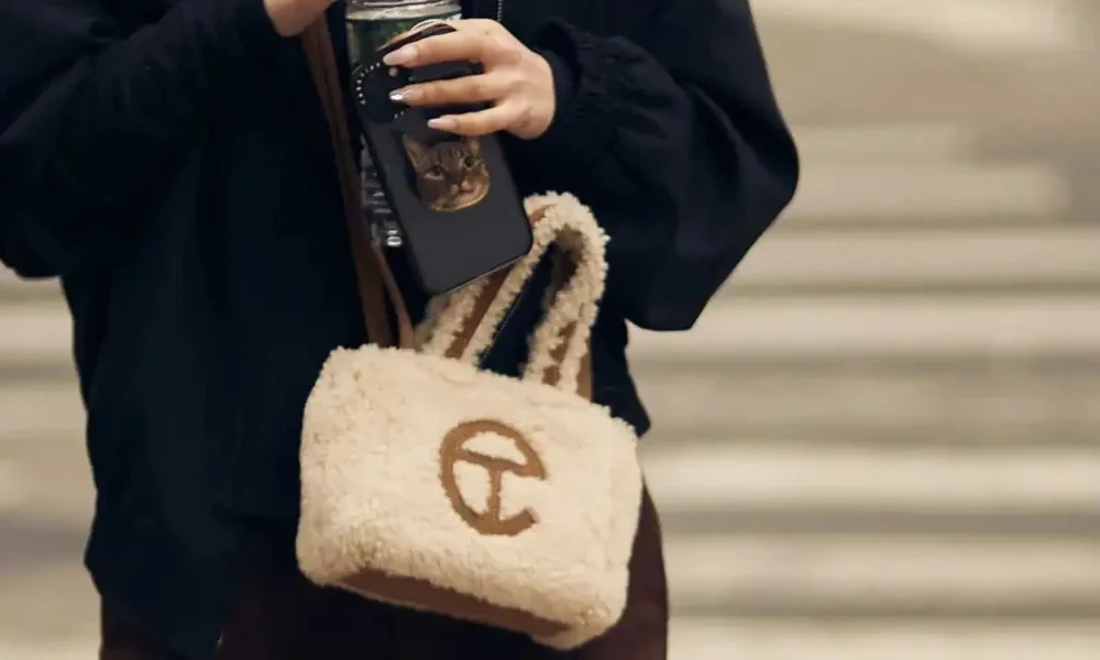 Person holding phone with cat popsocket and Telfar bag