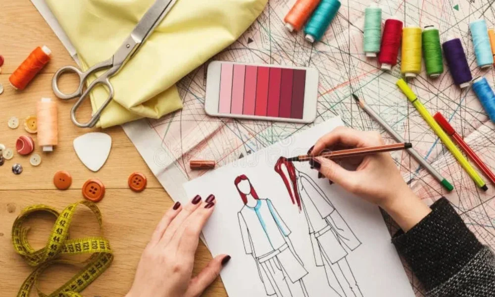 Hands coloring fashion sketches, surrounded by sewing supplies