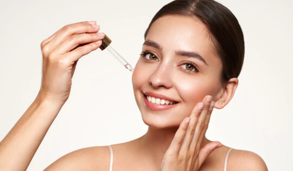 Woman applying facial serum with dropper, smiling