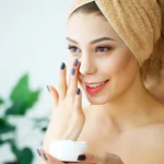 Woman with towel applying face cream to skin