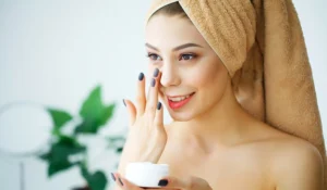 Woman with towel applying face cream to skin