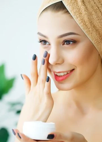 Woman with towel applying face cream to skin