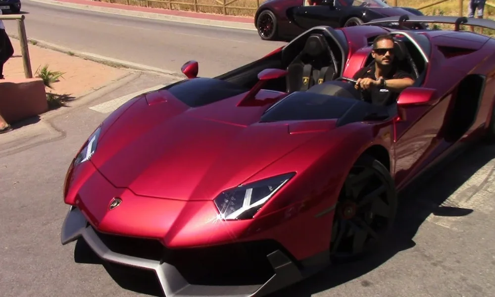 man in sunglasses driving a red lamborghini
