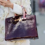 Person in embroidered jacket holding crocodile bag