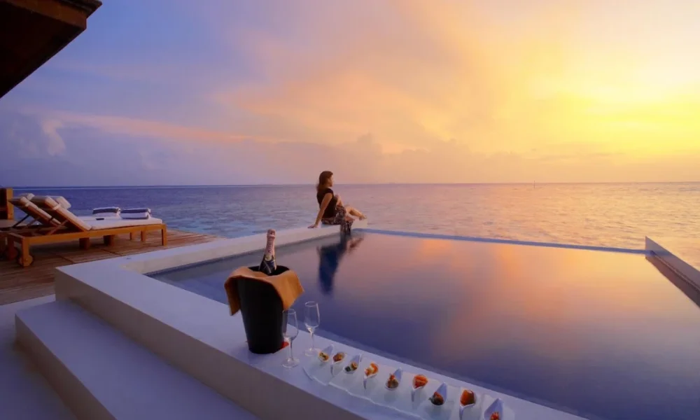 Woman by infinity pool at sunset with champagne