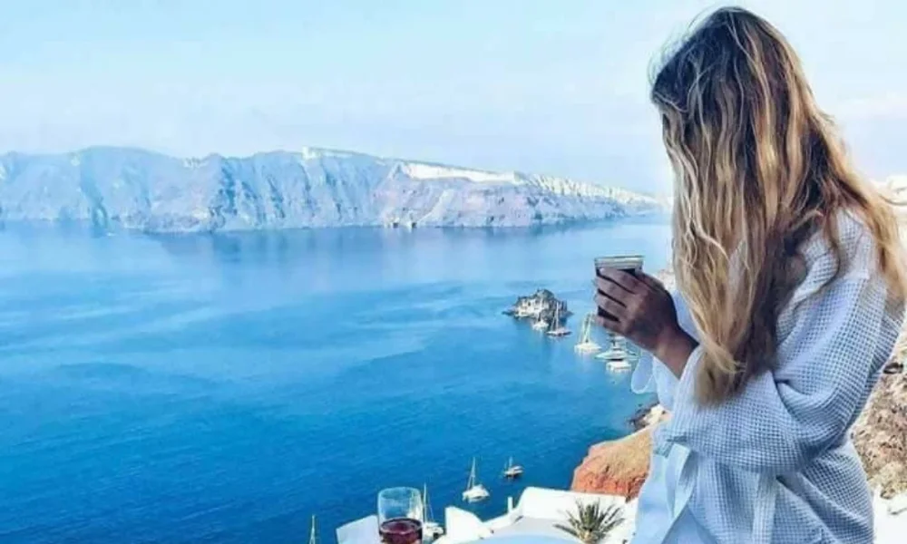 Woman in robe holding drink overlooking sea and mountains