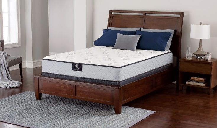 Classic dark walnut wooden platform bed setup with a plush multi-layer mattress, navy blue pillows, and matching minimalist wood nightstand with lamp