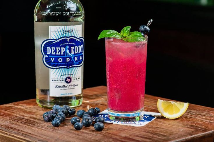 Glass of orange cocktail next to a bottle of Deep Eddy vodka.