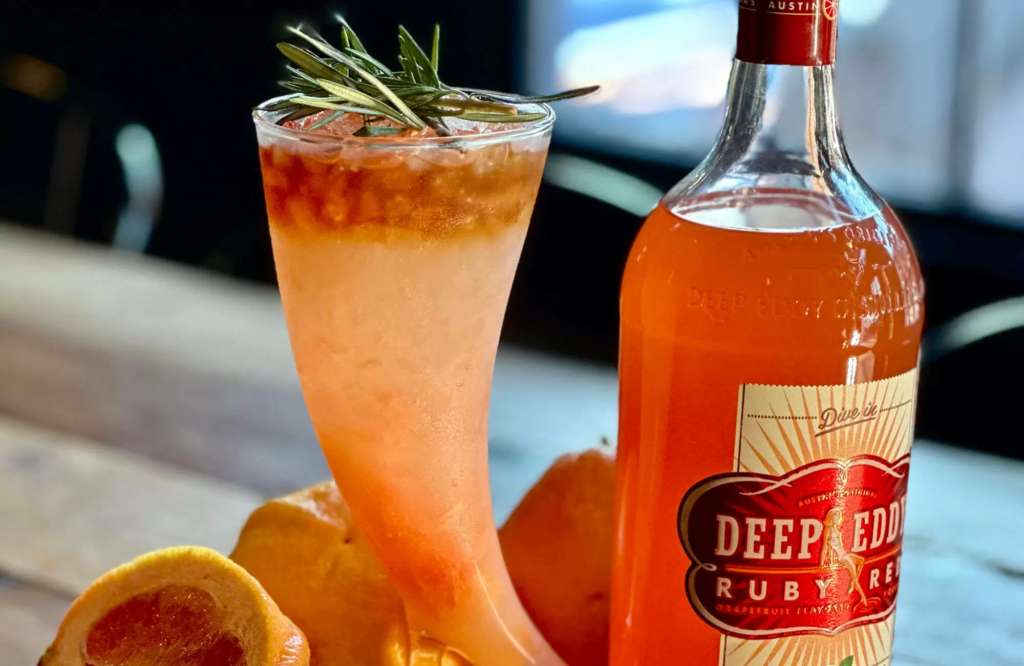 Glass of orange cocktail next to a bottle of Deep Eddy vodka.