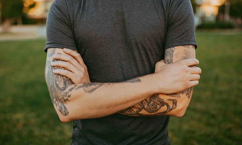 Man with crossed arms displaying detailed forearm tattoos.