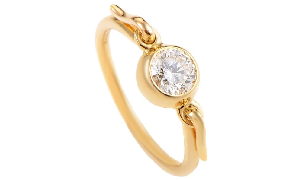Gold ring with a bezel-set diamond and unique clasp detail.