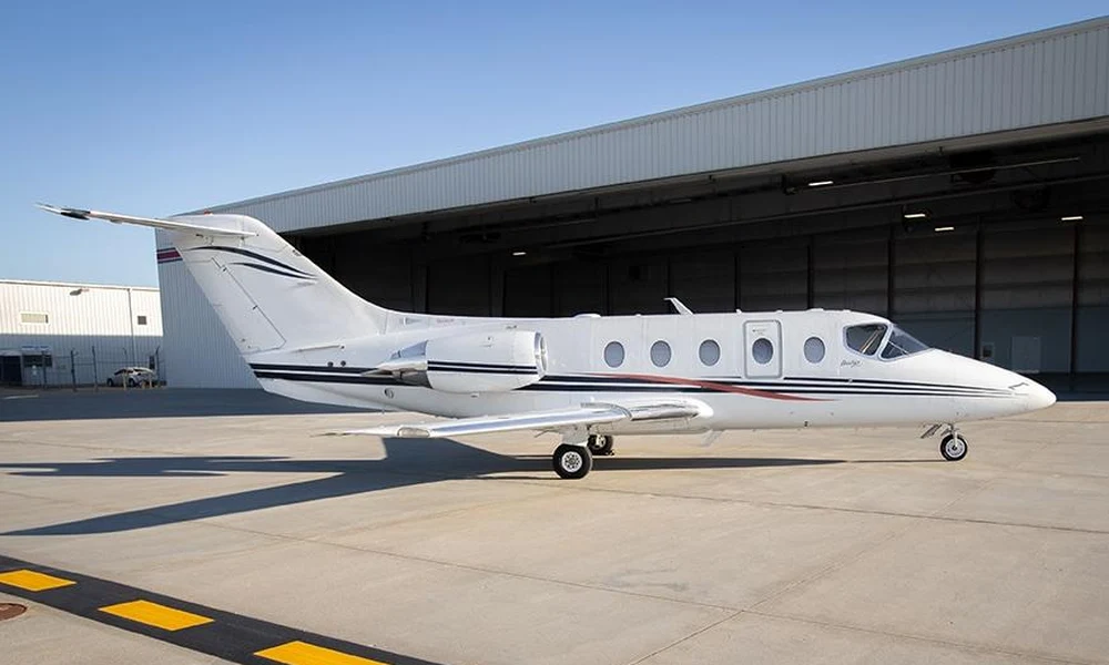 Compact light business jet parked on the tarmac in front of a open gray hangar building