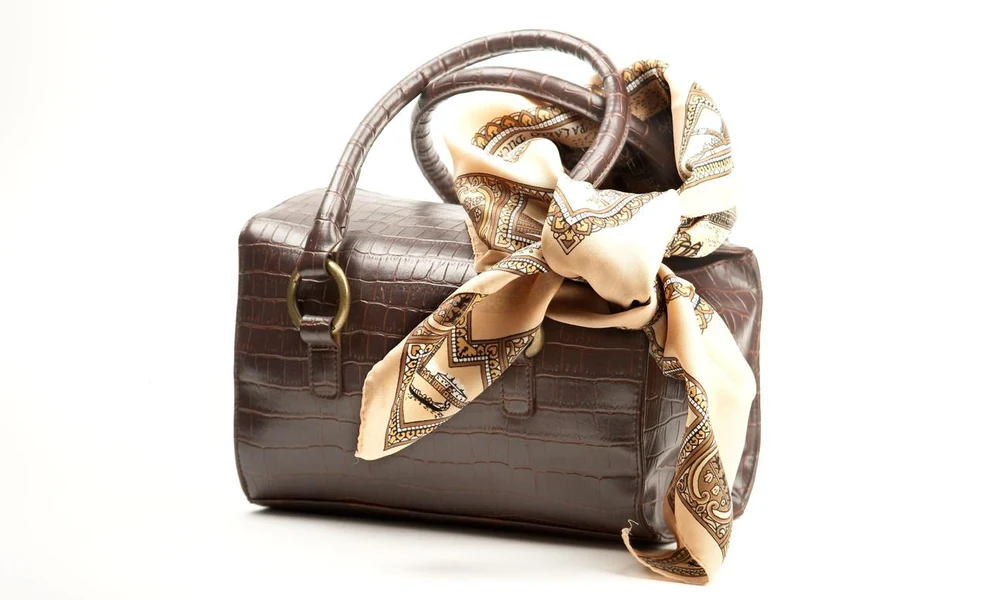 Brown leather handbag styled with a printed silk scarf tied to the handle.