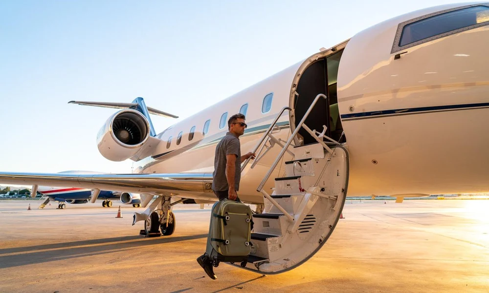 Passenger carrying a carry-on suitcase while stepping up the airstair door of a private aircraft-How to Fly Private