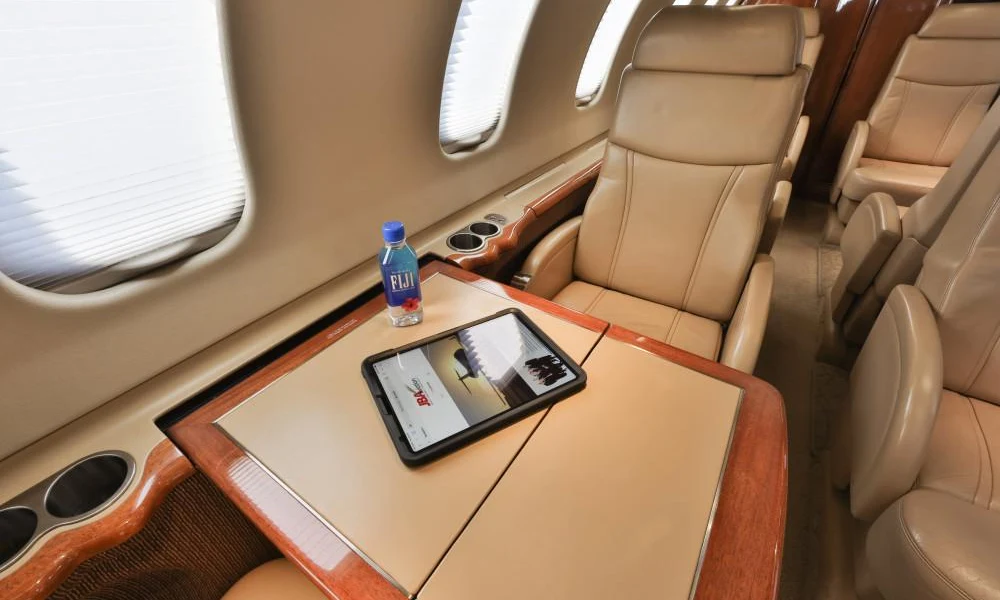 Fold-out wooden cabin table featuring a tablet computer and a bottle of Fiji water beside leather seats