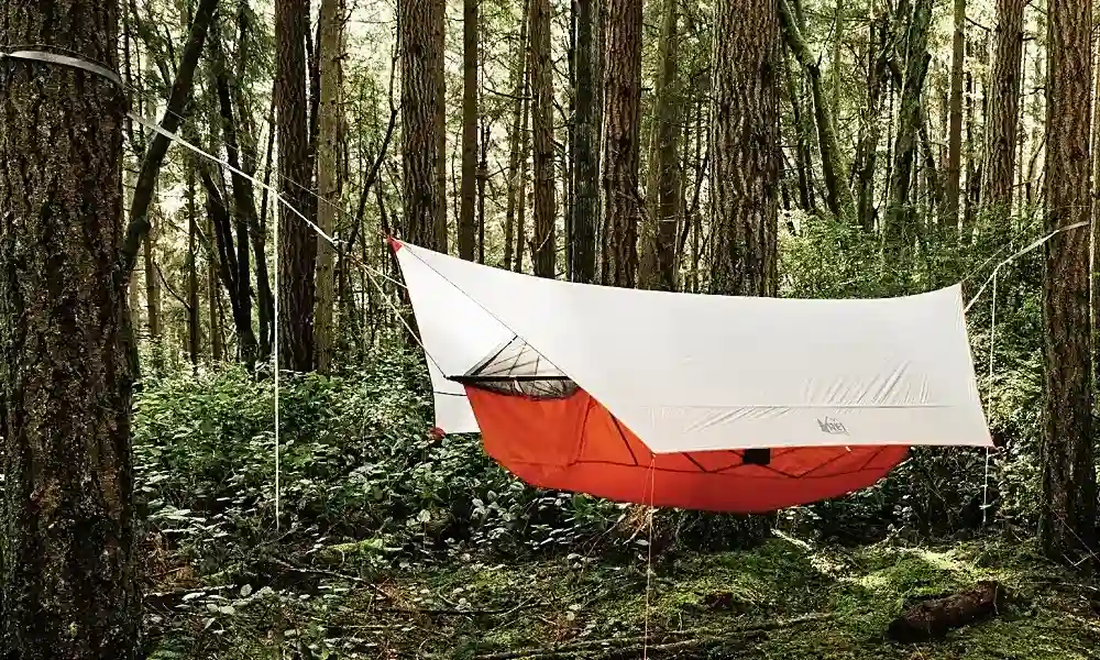 orange camping hammock set up with an integrated bug net and a white rainfly tarp overhead-best-camping-hammocks