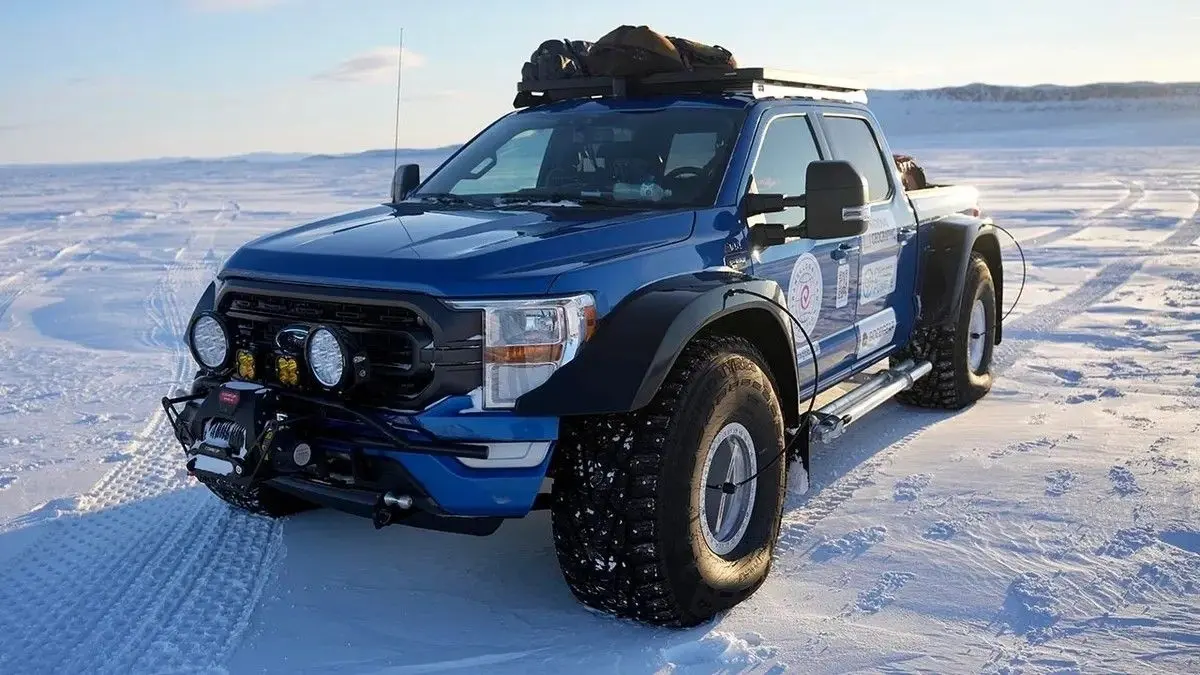 A blue off-road pickup loaded with roof gear stands on a snowy plain; deep tire tracks evoke a rugged, quiet winter expedition.