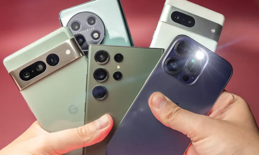 A hand fans out five premium smartphones with varied rear camera designs against a pink backdrop, highlighting sleek colors and modern technology.