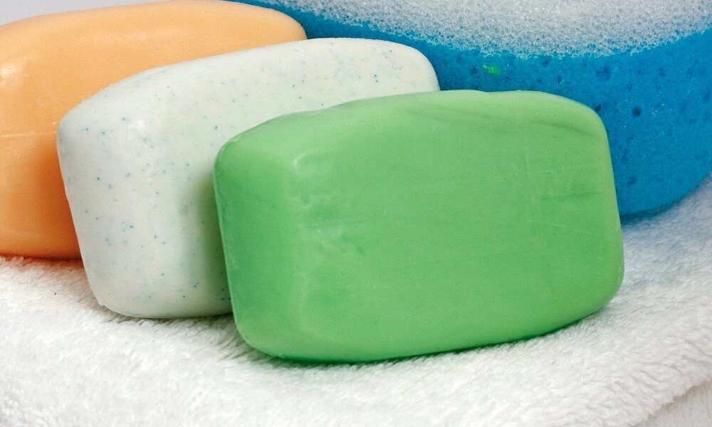 Four colorful bars of soap—green, white-speckled, orange, and blue—rest on a soft white towel, creating a clean, fresh, spa-like impression.