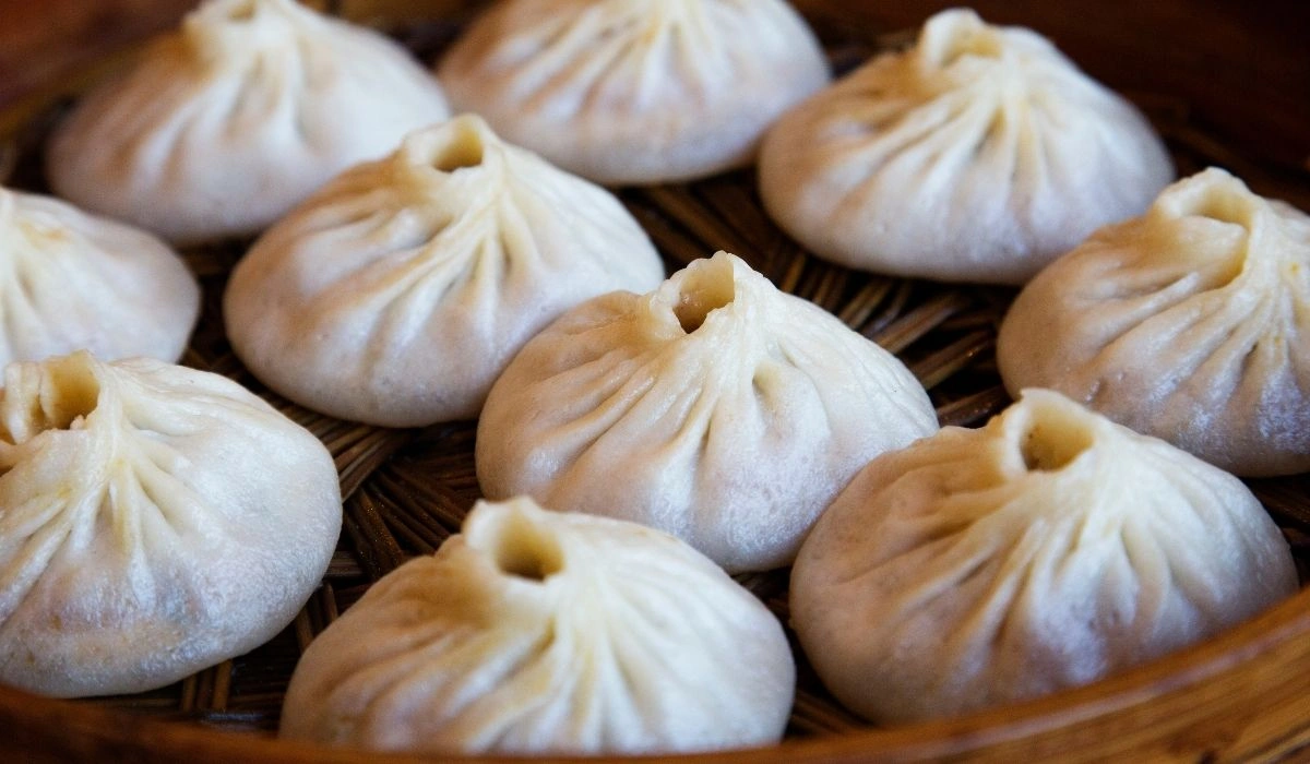 Close-up of plump white steamed dumplings with pleated tops arranged in a woven bamboo steamer, evoking a warm, appetizing traditional meal.