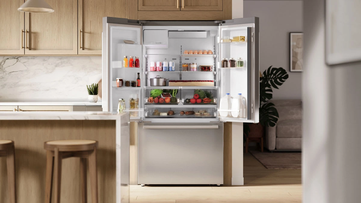 A modern kitchen features an open stainless-steel refrigerator neatly stocked with colorful food, drinks, and fresh produce, creating a welcoming feel.