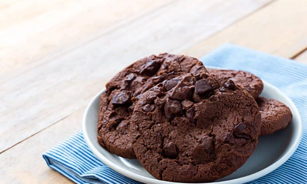 A white plate holds several large, rustic chocolate cookies-Best Chocolate Chip Cookie Recipe 2026