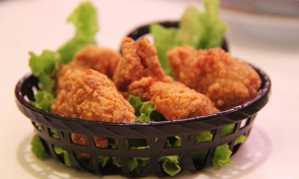 A black basket of golden, crispy fried chicken pieces sits on a plate, lined with fresh green lettuce; the appetizing presentation feels casual and inviting.