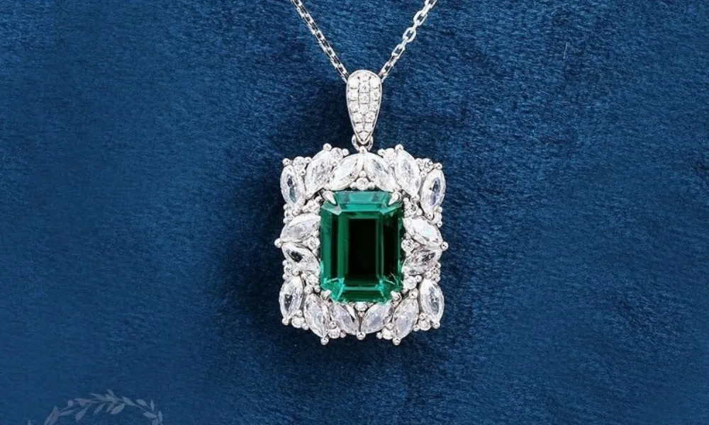 luxury diamond necklaces featured in a detailed view of a rectangular pendant with a center emerald-cut green stone surrounded by a marquise diamond halo on a navy blue backdrop.