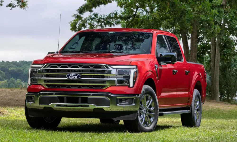 A polished red Ford F-150 pickup truck with chrome grille and wheels is parked on grass beneath leafy trees, conveying rugged confidence and capability.