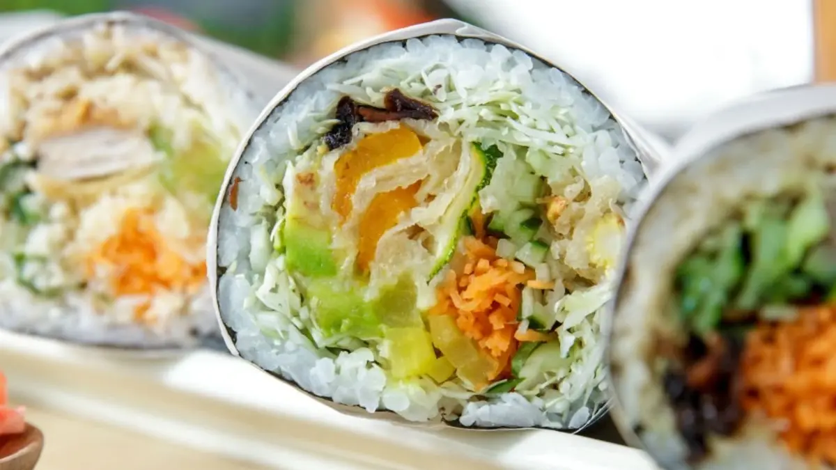 Close-up of sliced vegetable sushi rolls filled with rice, avocado, carrot, and greens, arranged on a platter; fresh, colorful, and appetizing.