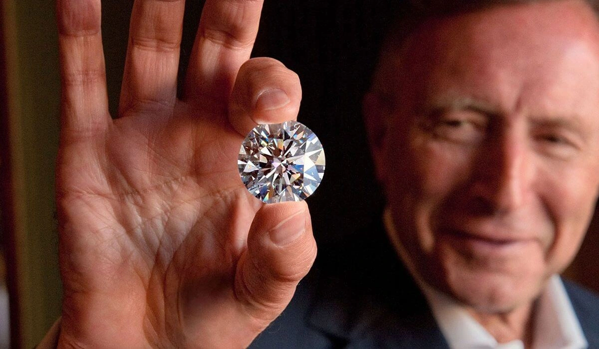 A man holding a large, round brilliant-cut diamond between his fingers.
