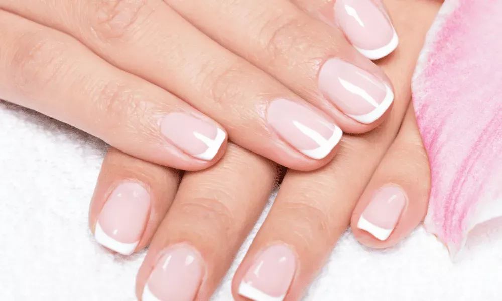 Close-up of manicured hands with glossy pale pink nails and crisp white French tips 