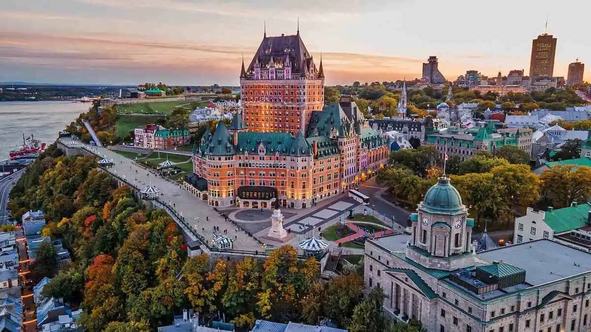 At sunset, Château Frontenac’s grand towers rise above Old Québec, with the St. Lawrence River, tree-lined streets, and historic rooftops below.