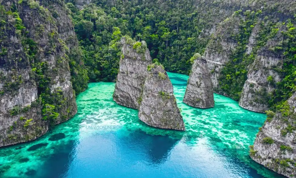 Aerial view of vivid turquoise water winding between towering limestone karst cliffs and forested islands, creating a serene, dramatic tropical scene.