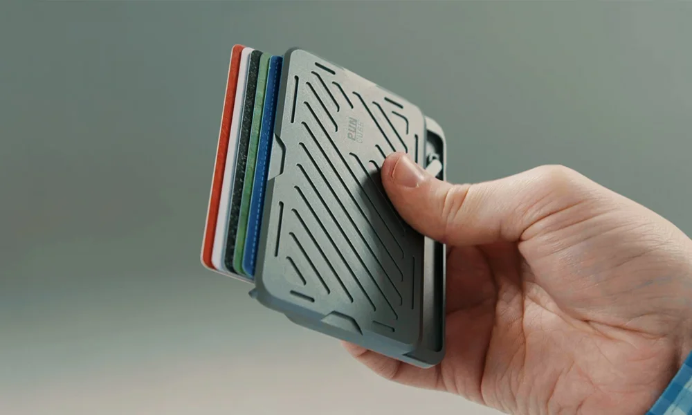 A hand holds a slim gray card wallet with textured diagonal grooves and colored cards