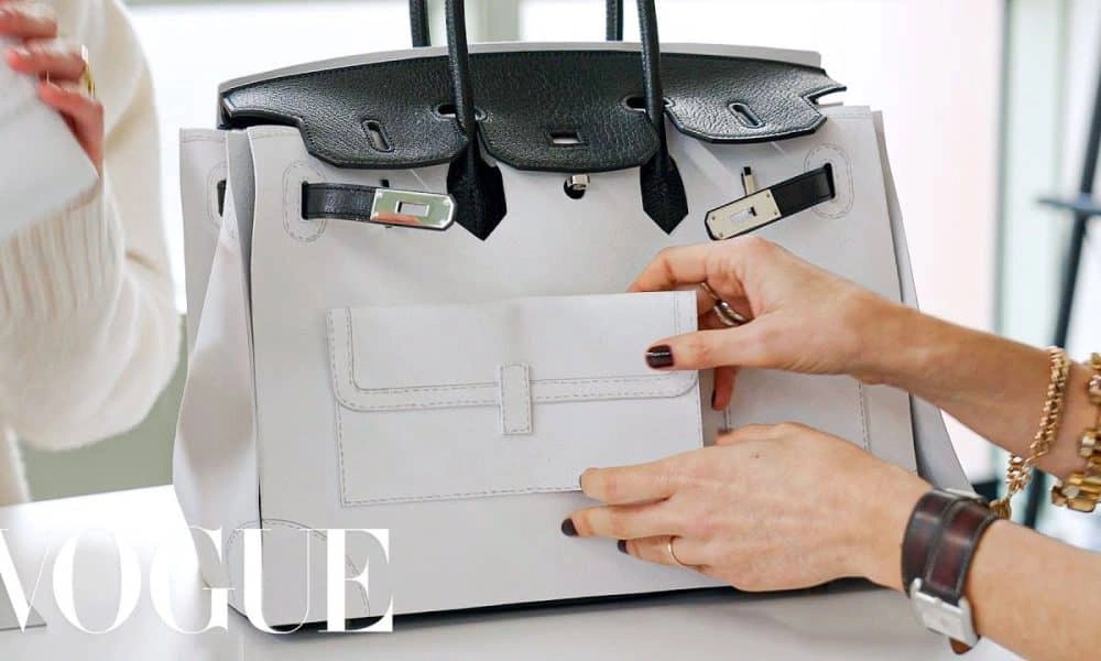 A woman’s hands display a structured light-gray designer handbag with black handles and silver hardware; a VOGUE watermark adds a polished fashion-editorial feel.