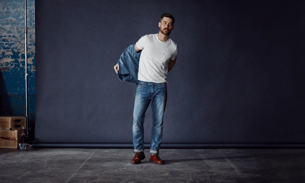 A bearded man in a white T-shirt and jeans slips off a denim jacket-Football Game Outfit Ideas