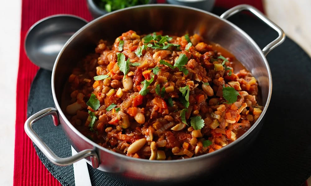 A stainless-steel pot brims with hearty tomato and bean stew, topped with fresh herbs-Best Chili Recipe
