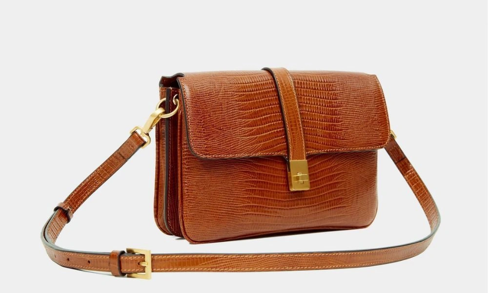 A structured cognac-brown leather shoulder bag with embossed texture, flap closure, gold-tone clasp, and adjustable strap, shown against a white background.