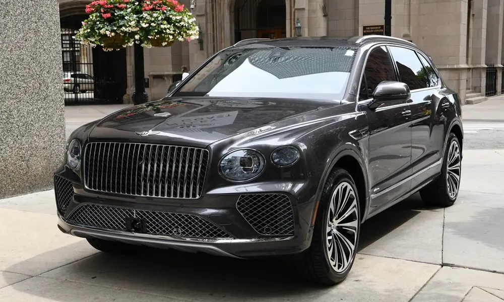 Dark metallic grey Bentley Bentayga luxury SUV parked outside a historic stone building