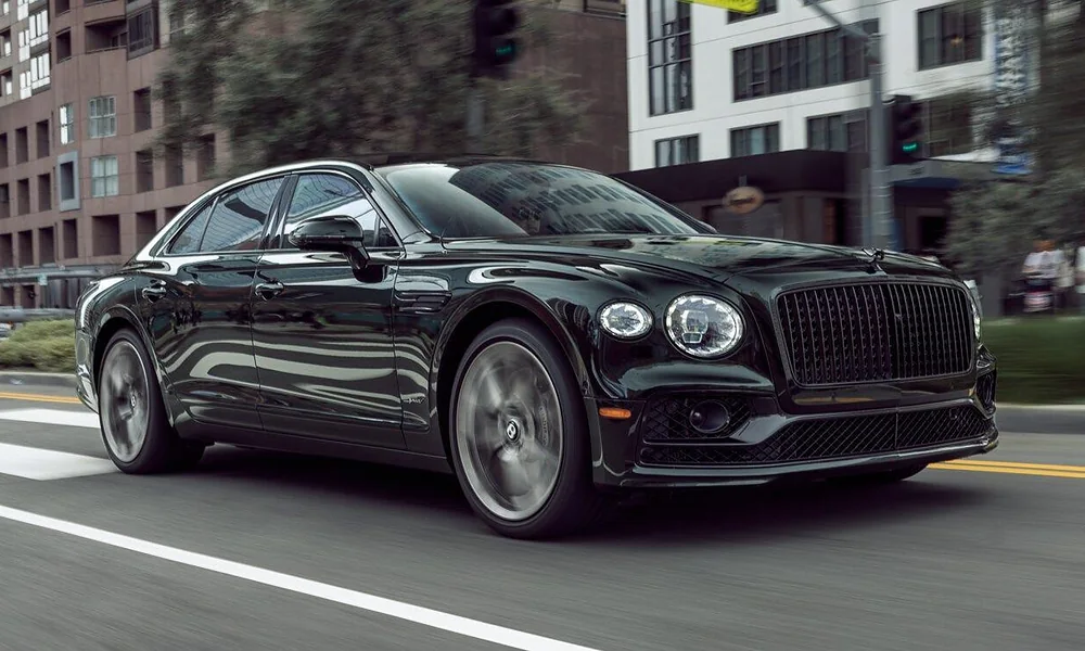 Glossy black Bentley Flying Spur sedan driving dynamically along an urban city street