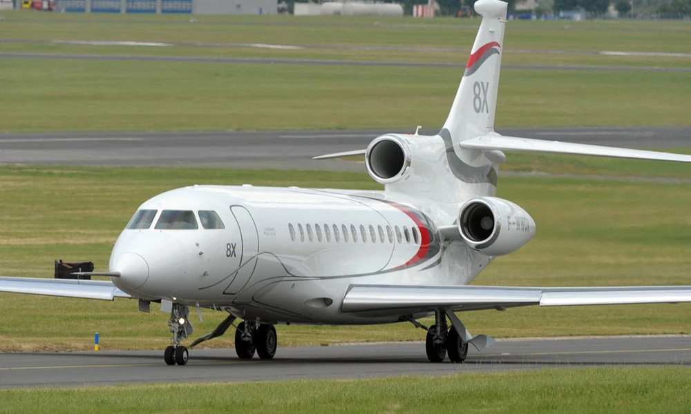 Dassault Falcon 8X tri-jet taxiing along an airport runway near green fields